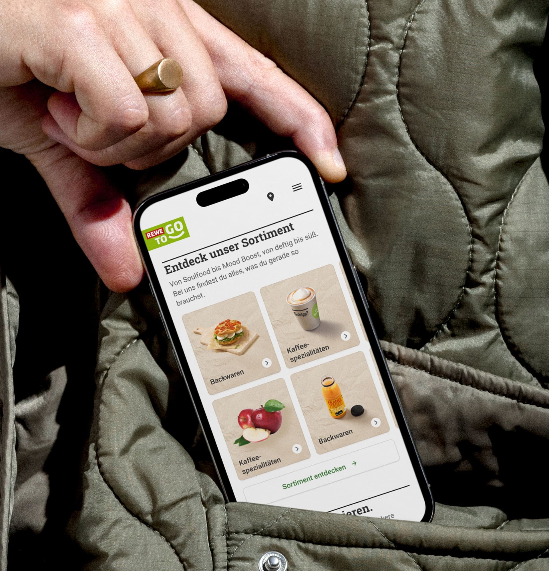 Close-up of a hand holding a smartphone displaying the REWE To Go website