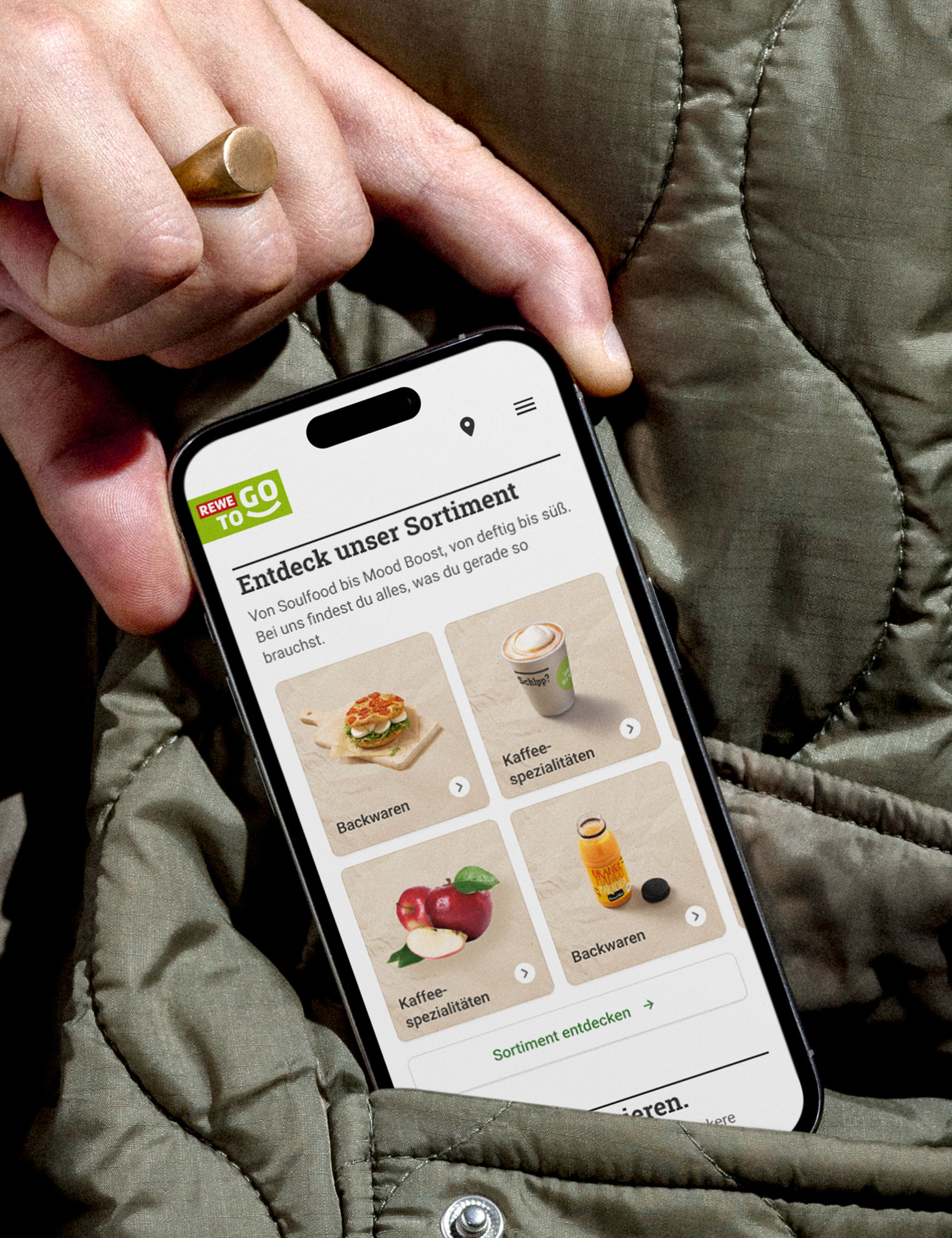 Close-up of a hand holding a smartphone displaying the REWE To Go website