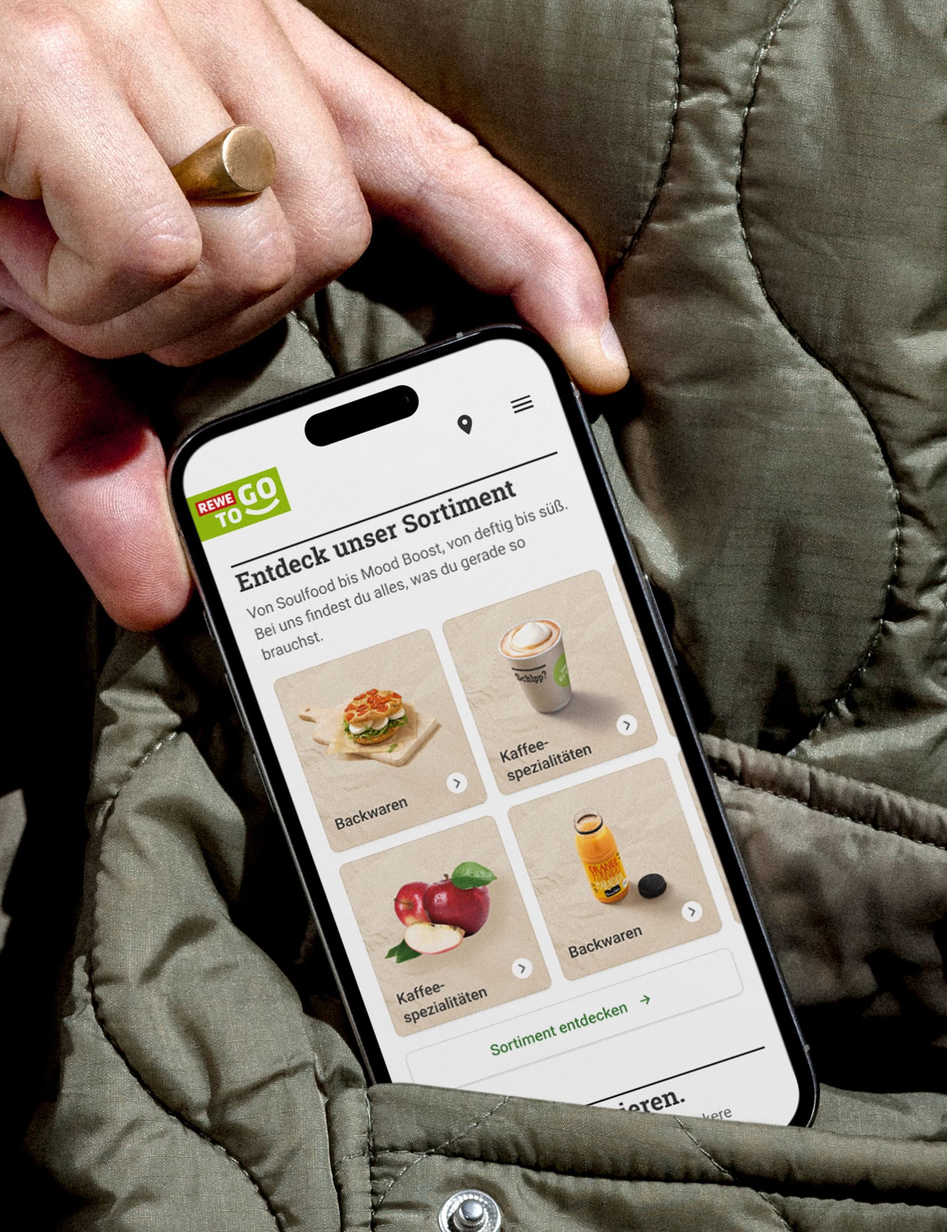 Close-up of a hand holding a smartphone displaying the REWE To Go website