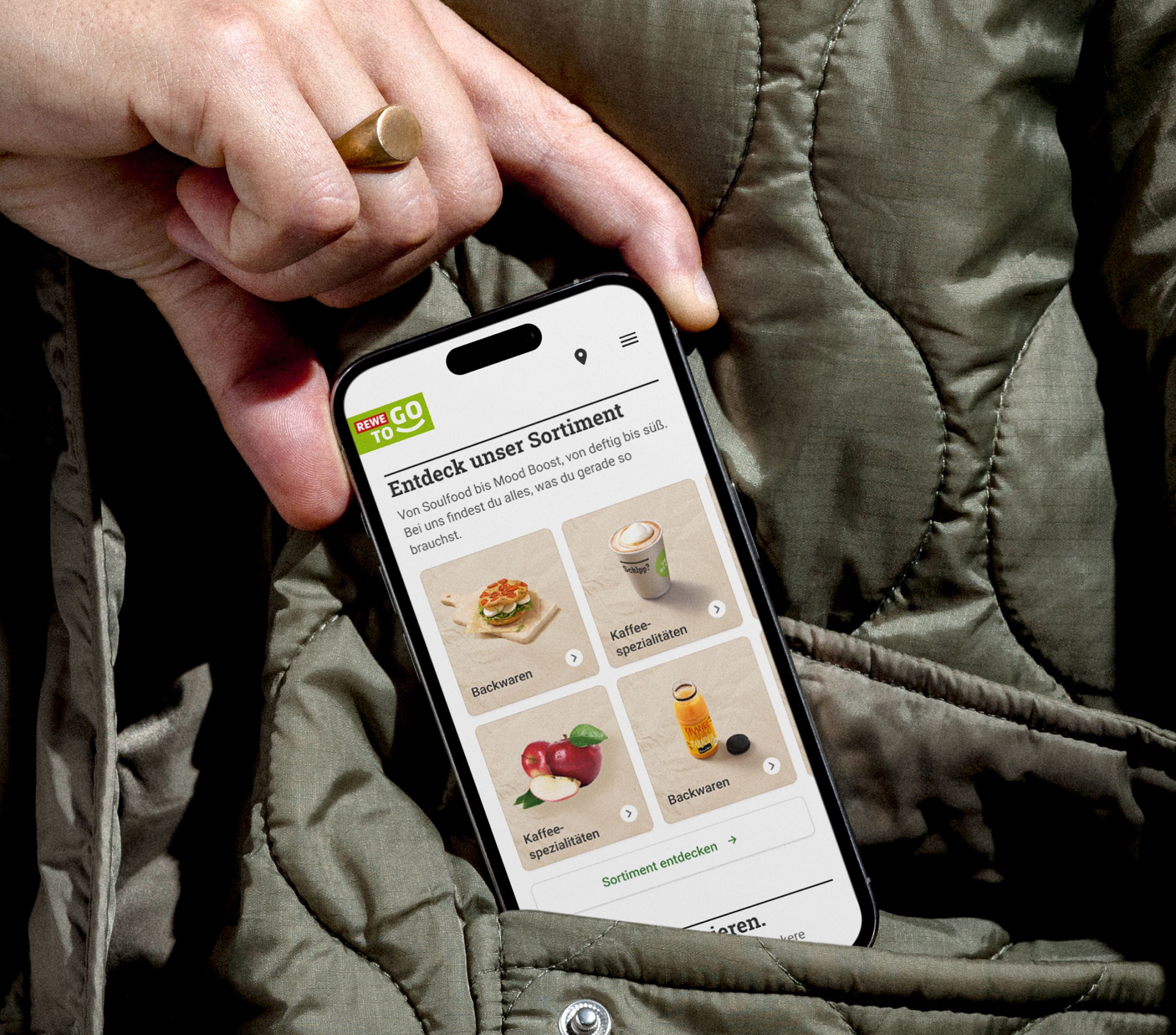 Close-up of a hand holding a smartphone displaying the REWE To Go website