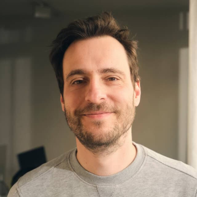 Person with short brown hair and a beard, wearing a grey sweatshirt indoors